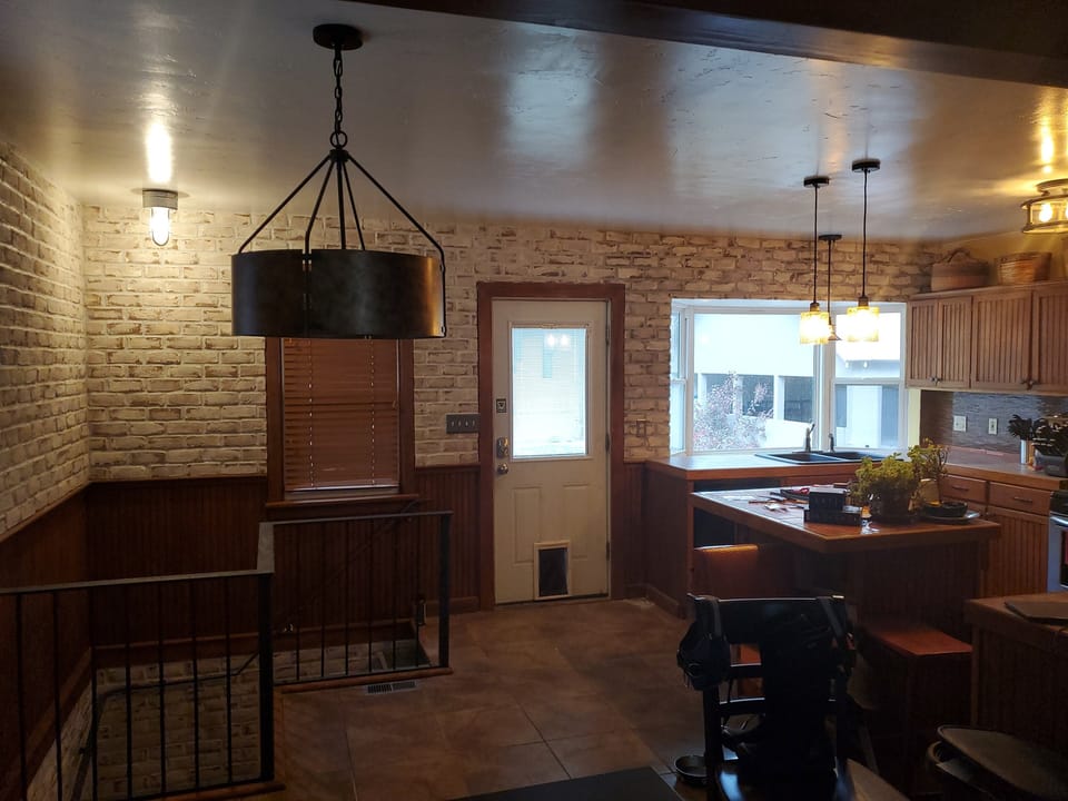 Same kitchen wall faced in pale brick above the wood wainscot, brick carried down the open stairwell