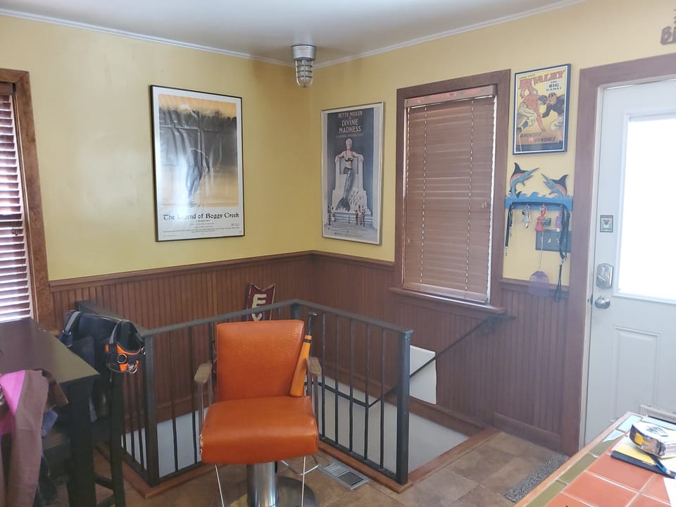 Plain yellow painted wall above wood wainscot in a kitchen corner with framed posters and an open stairwell