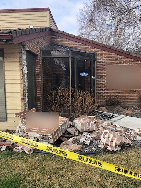 Brick entry wall toppled by a car, broken brick and cap slabs behind fire line tape