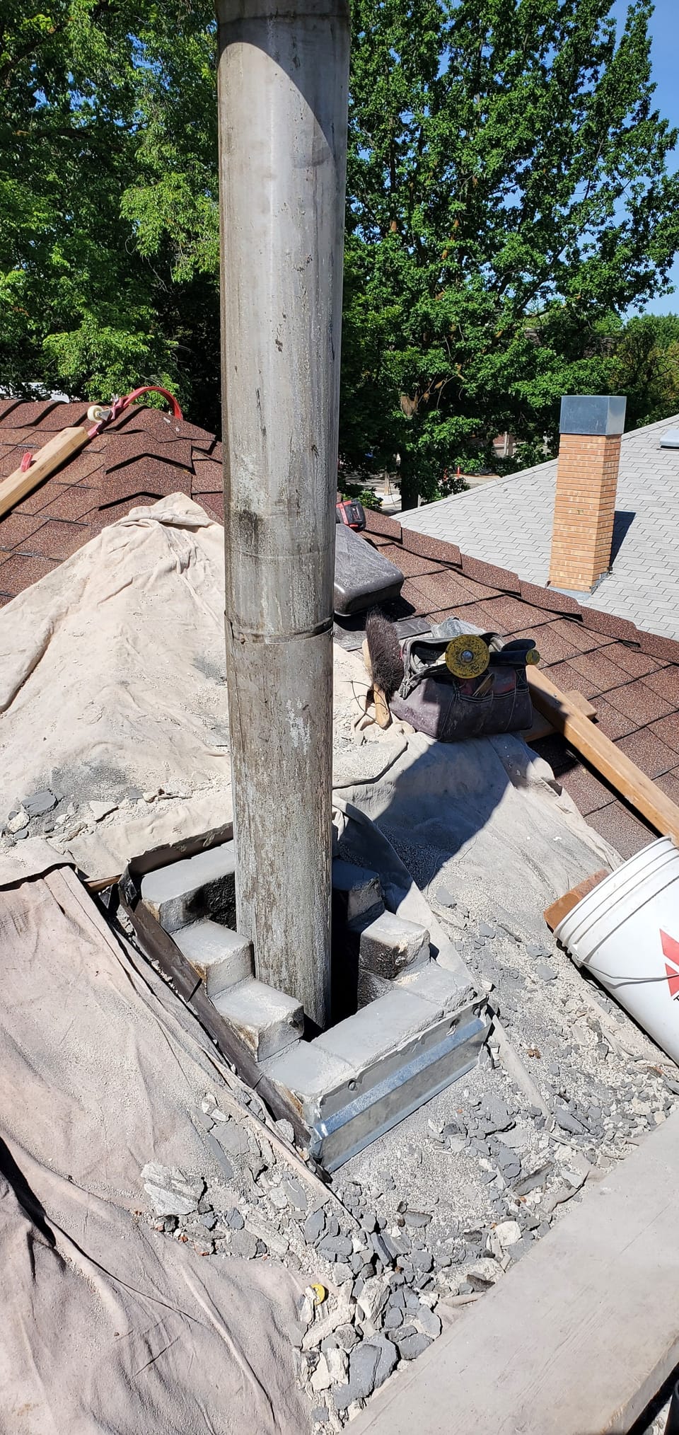Chimney demolished to the roofline around the metal flue pipe, shingles tarped and rubble cleared