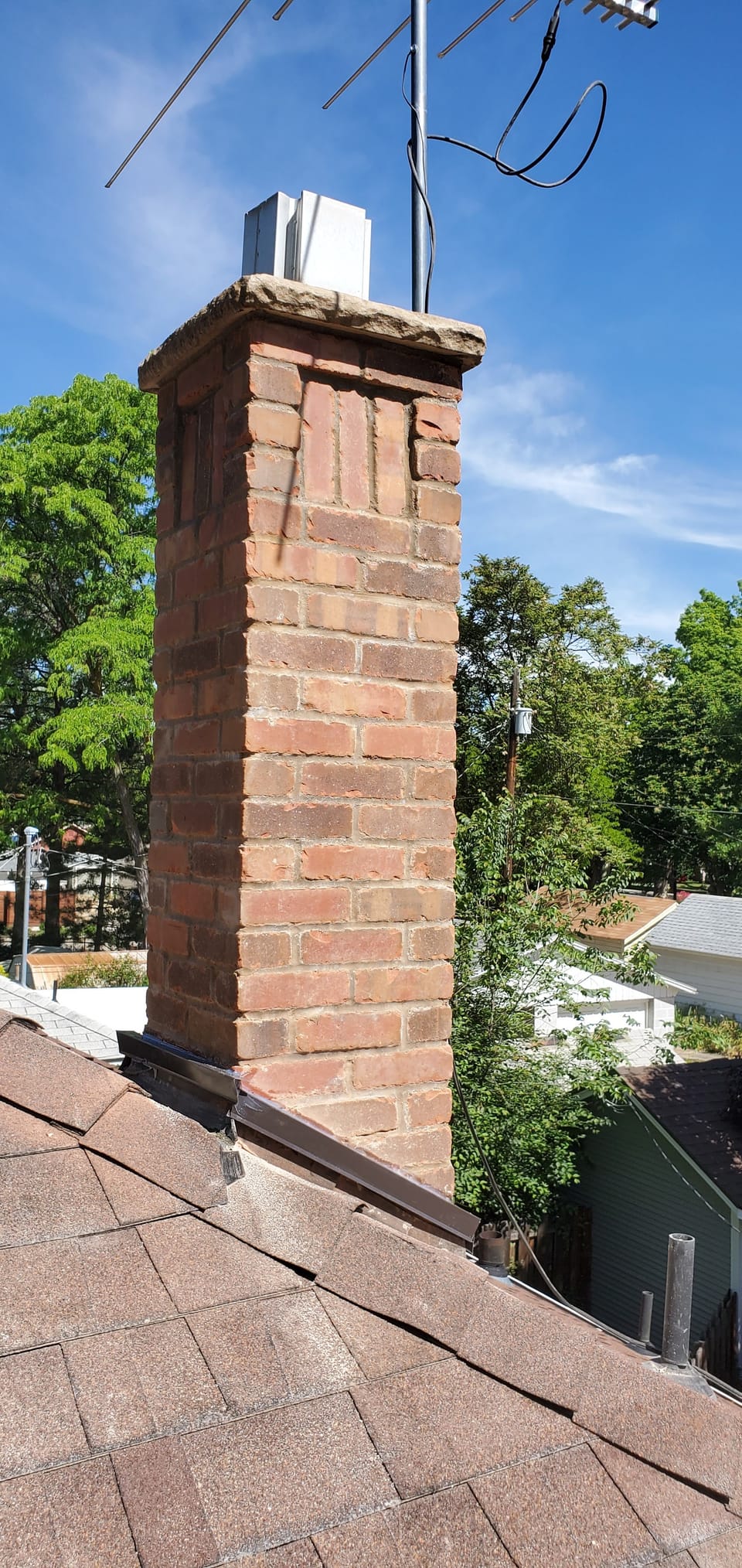 New brick chimney with a recessed panel and stone cap, fresh flashing where it meets the shingle roof