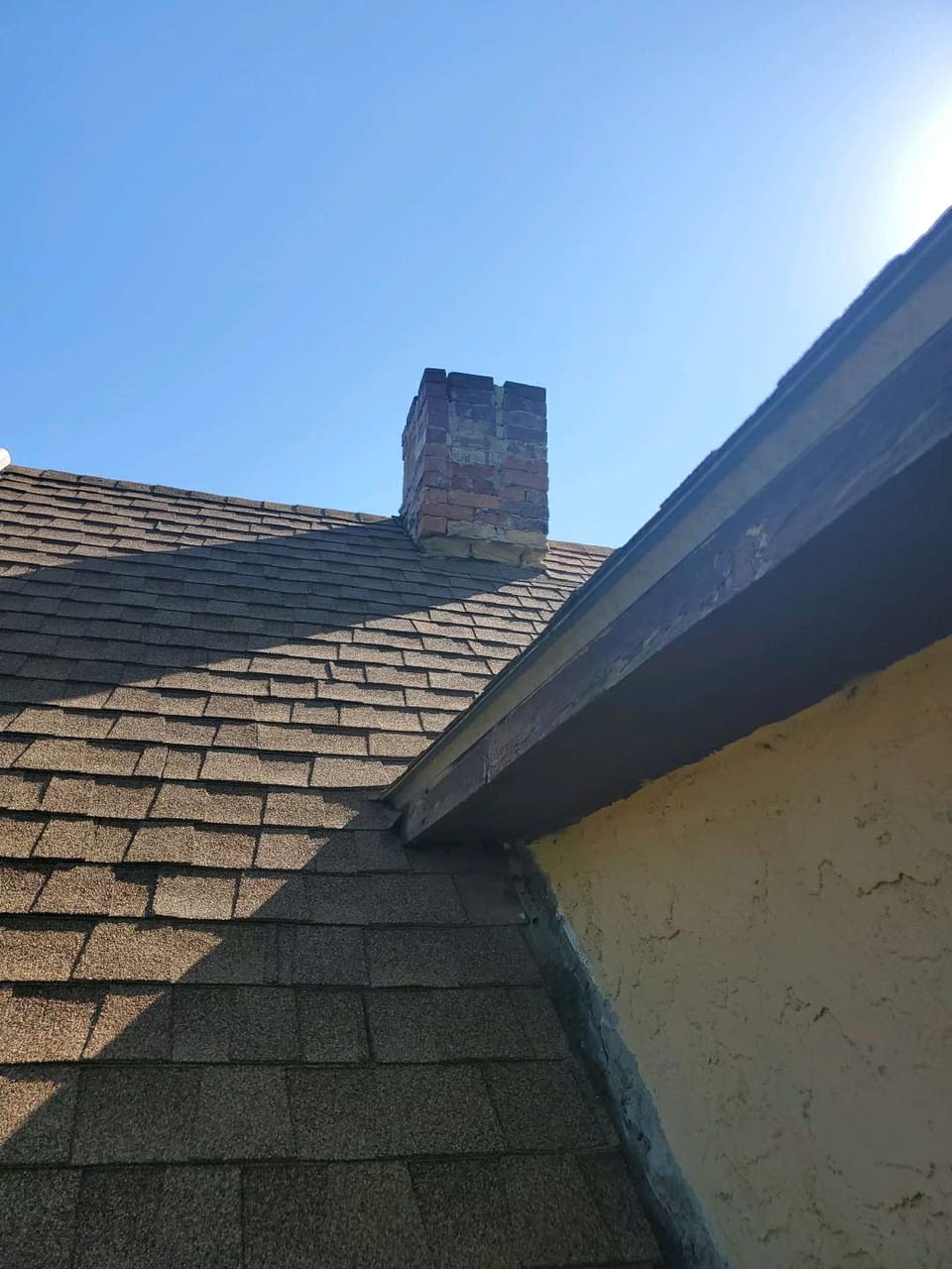 Short deteriorated brick chimney with crumbling faces and loose top courses above a shingle roof