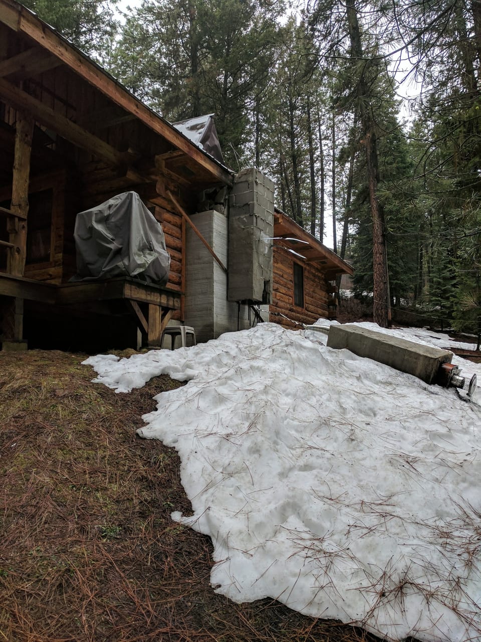 Log cabin with its block chimney broken off at the roofline and the cap lying in snow