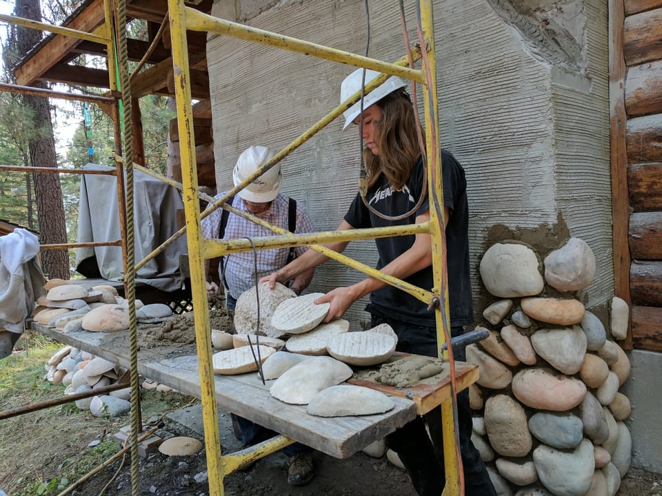 Apprentice choosing a manufactured river rock off the sorting plank as the first courses go up