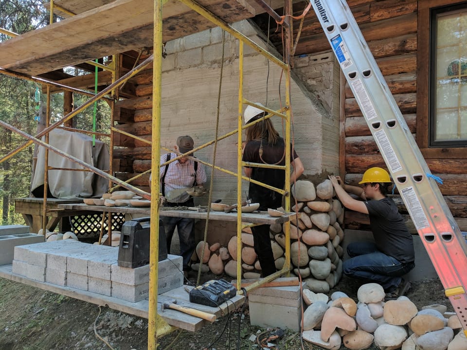 Manufactured river rock veneer climbing the chimney chase while stone is cut and set from the scaffold plank