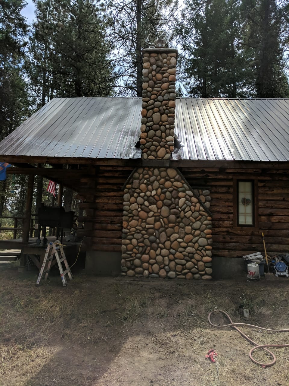 Completed manufactured river rock chimney running from the ground to the cap up the log cabin's metal roof