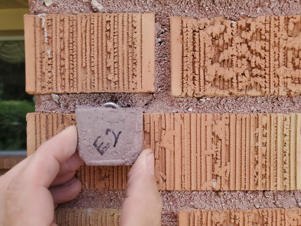 Cured mortar sample held against a brick wall to compare its color against the existing joints