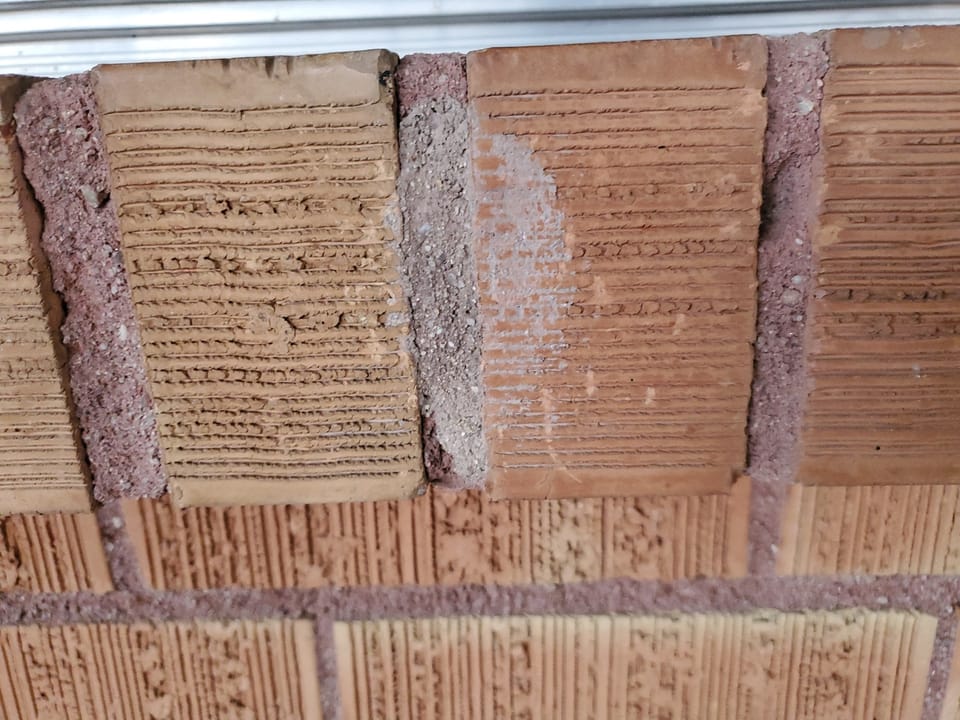 Close-up of brick with gray mortar smeared across the face from an earlier repair