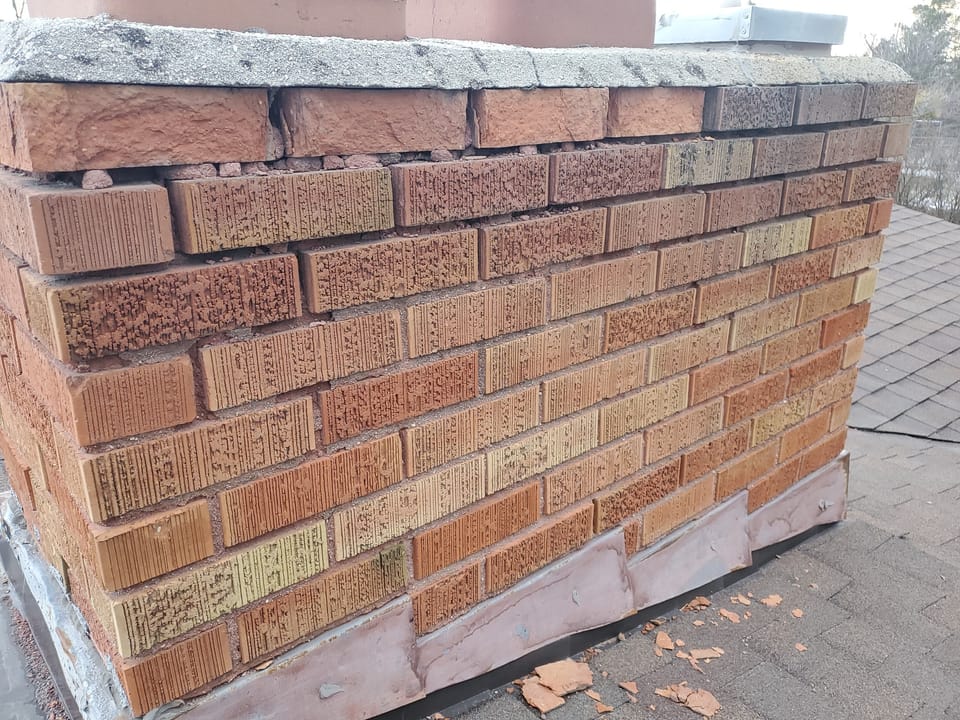 Deteriorated brick chimney before repair with eroded mortar joints, spalled brick and a cracked concrete cap