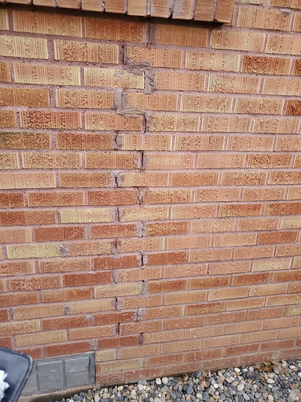 Stair-step crack running down a brick wall, crudely filled with mortar by a previous repair