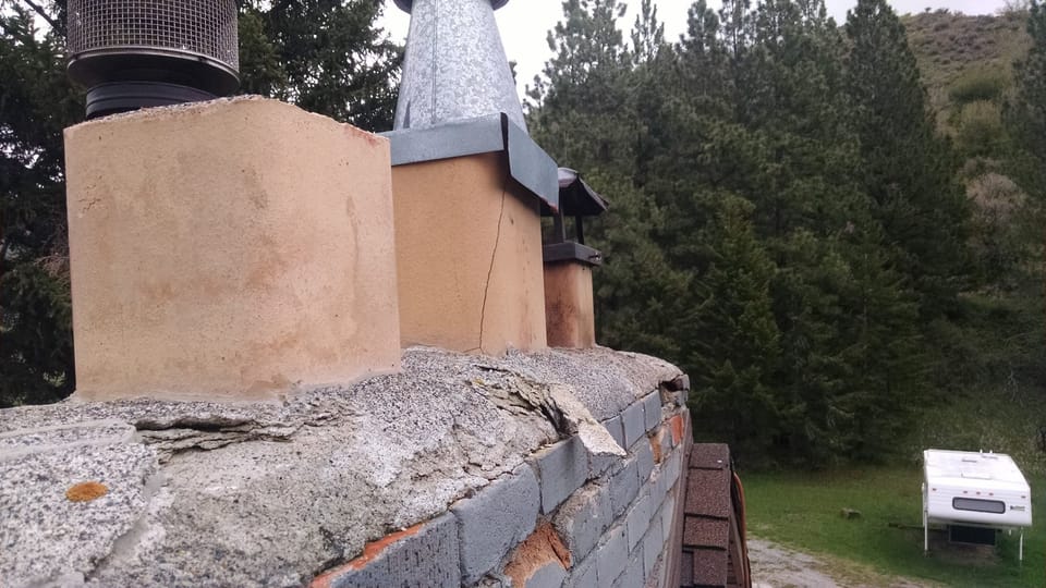 Crumbling concrete cap breaking apart on top of a painted brick chimney above the roof