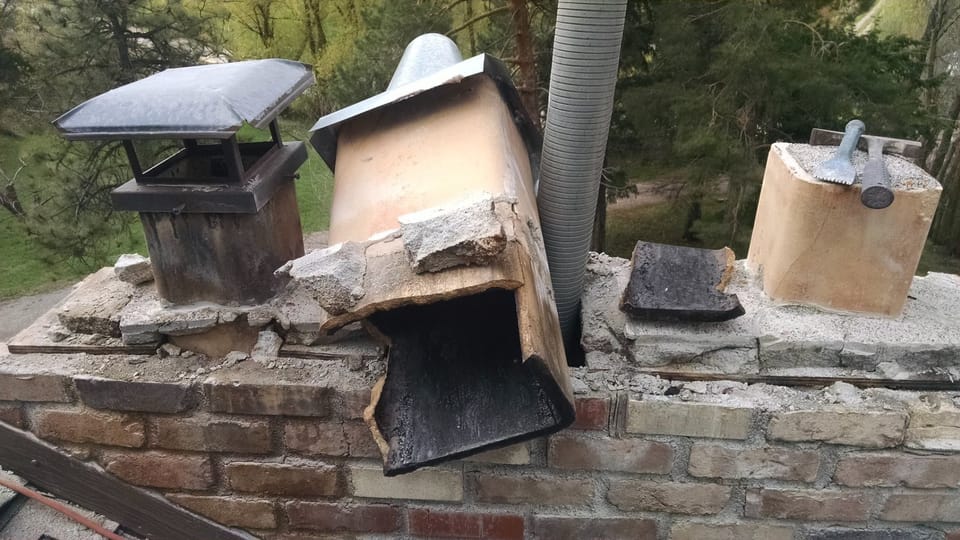 Weathered clay flue liner and removed cap on the chimney top, chisels resting alongside