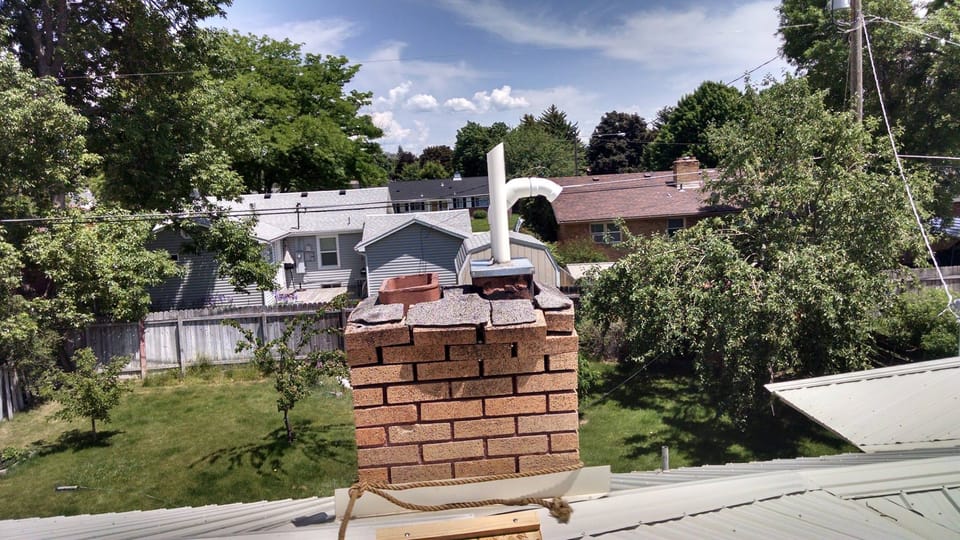 Brick chimney above a metal roof with a broken cap and loose top courses of brick sitting unbonded