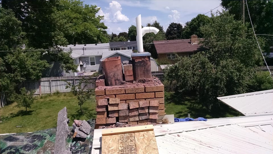 Chimney with cap and loose brick removed, two clay flue liners standing exposed above crumbling mortar