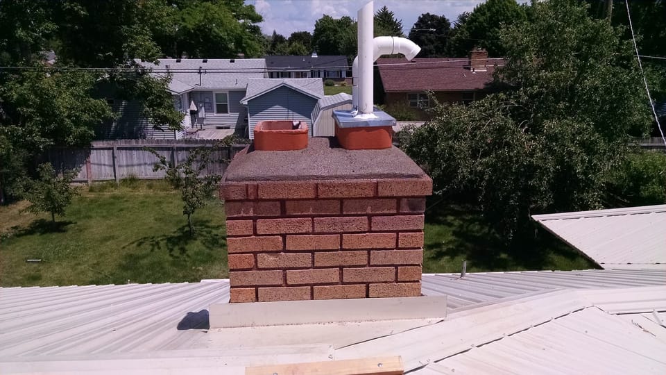Rebuilt chimney top with a new sloped cap, drip edge and repaired top liner section above the metal roof