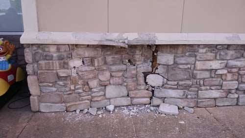 Stone veneer wainscot punched through and cracked where a car struck the storefront, rubble on the sidewalk