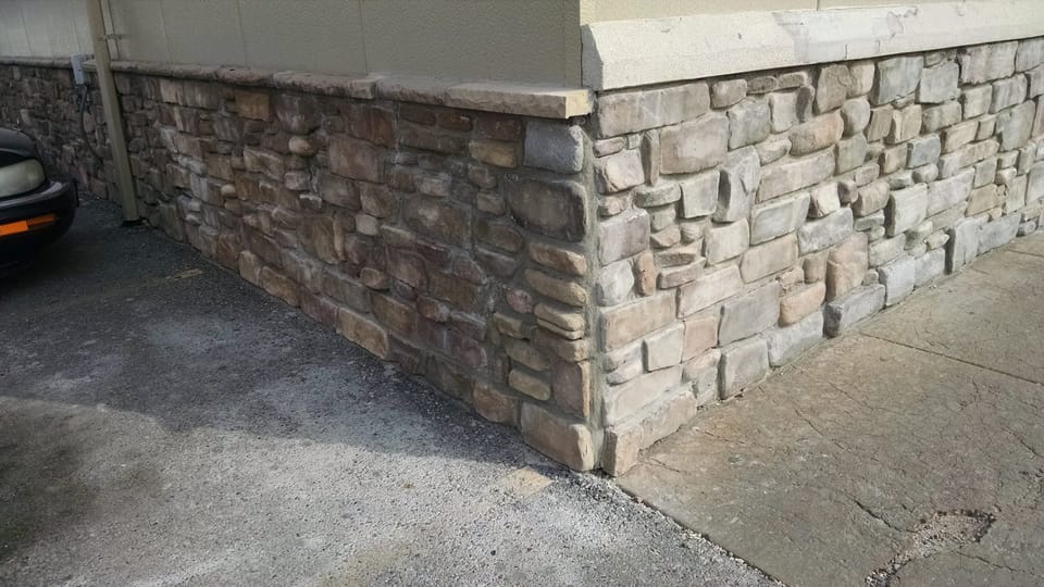 Repaired building corner where the new stone meets the original weathered veneer under a cap