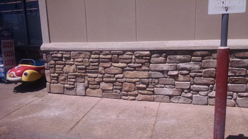 Rebuilt stone veneer wainscot with a concrete cap outside the store entrance, joints struck clean