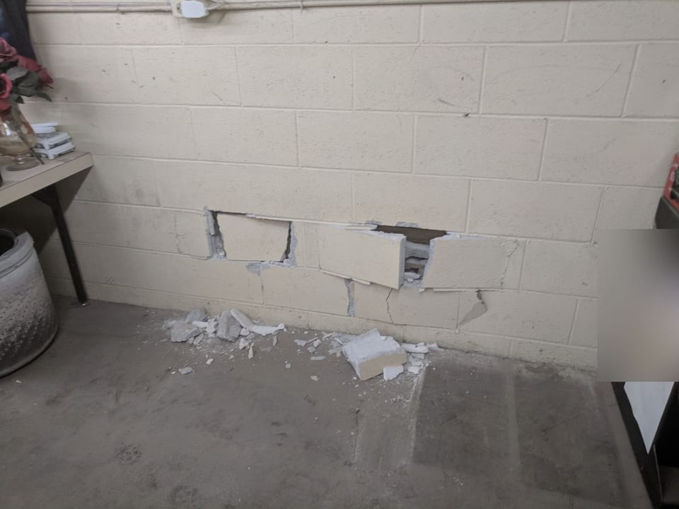 Painted block wall seen from inside, cracked and shoved inward where forklift forks punched through