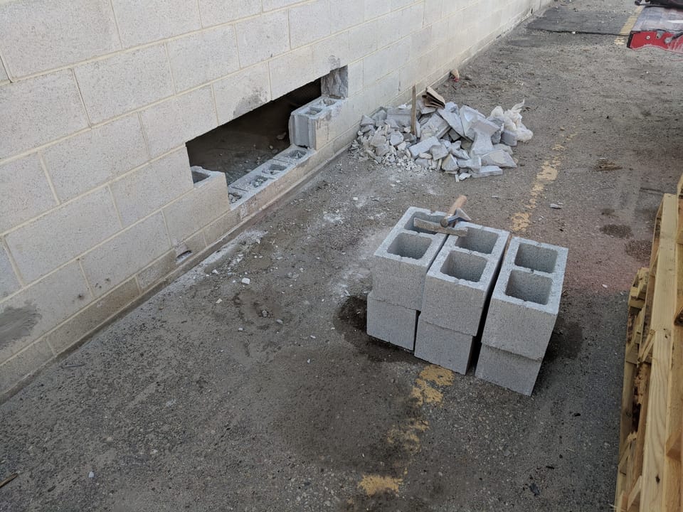 Damaged block cut out of an exterior concrete block wall, broken pieces and new blocks nearby