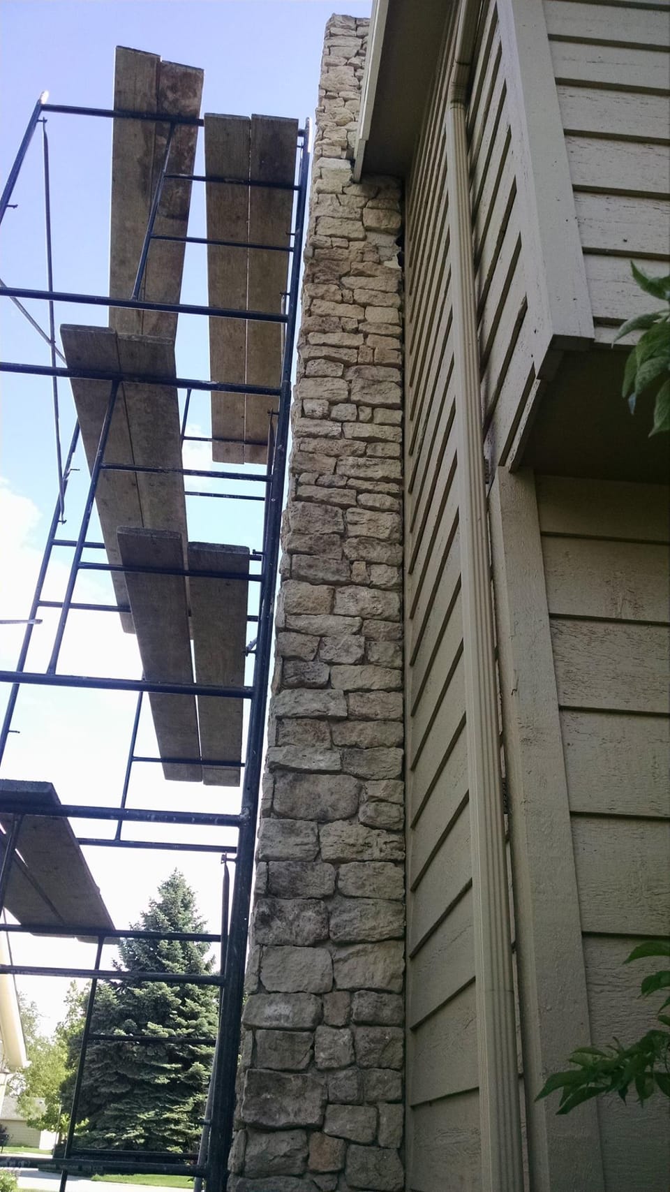 Tall light stone chimney running up the side of a sided house with scaffold planks standing alongside