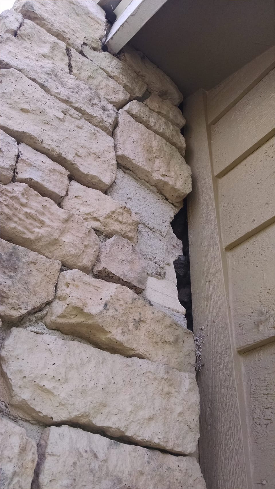 Open gap between the stone chimney and the house corner trim, mortar cracked and stones pulled apart
