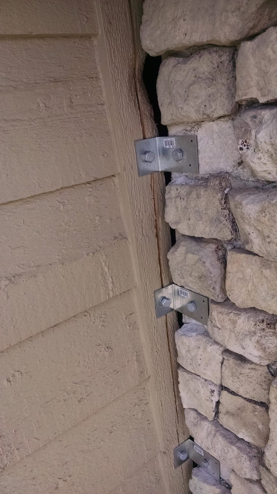 Galvanized angle brackets bolted across the open gap between the stone chimney and the house siding