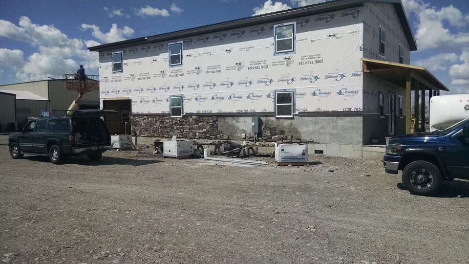 Stone veneer going up along the base of a housewrapped commercial building, pallets of stone on site