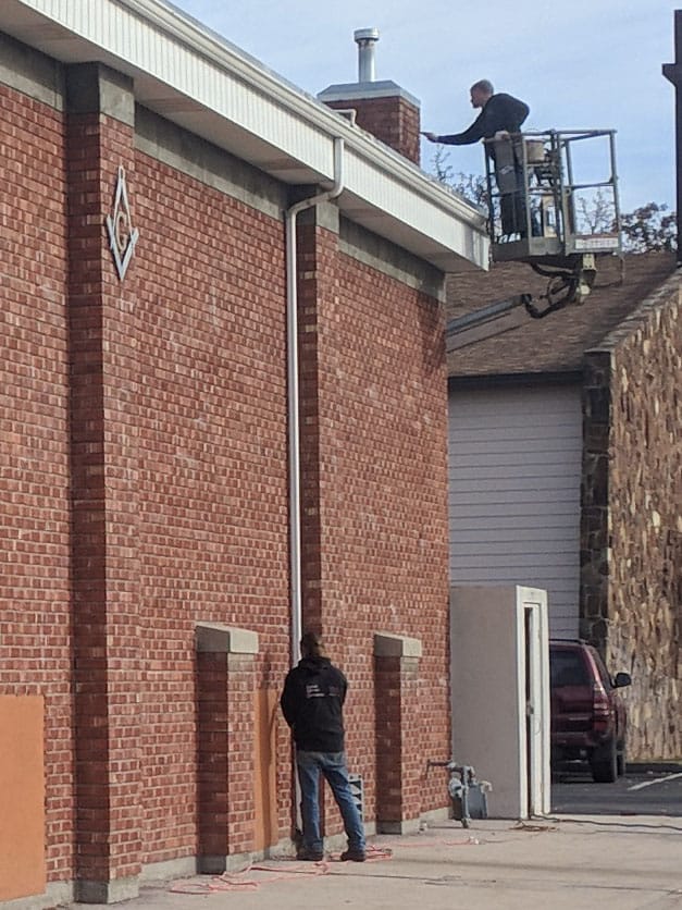 Mason in a lift working at the roofline chimney of the Meridian Masonic Temple, another kneeling below