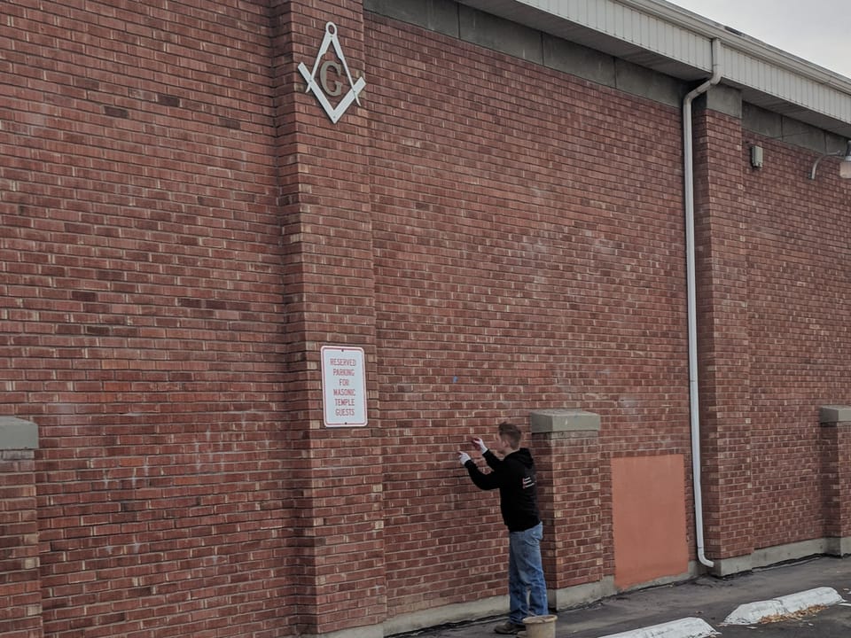 Mason pointing joints low on the brick wall below the Masonic square and compass emblem in Meridian