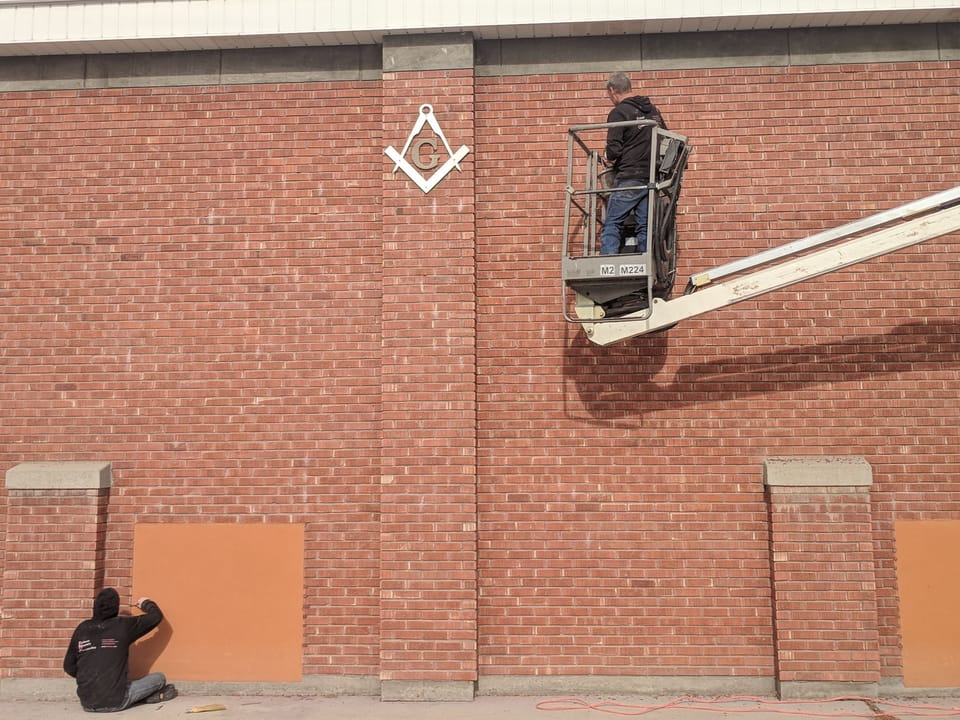 Two masons repairing the Meridian Masonic Temple brick, one in a boom lift, one kneeling at the base