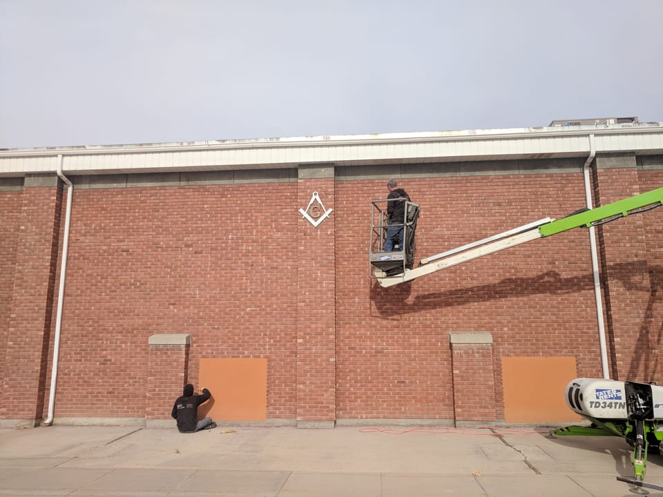 Green boom lift raised against the tall brick wall of the Meridian Masonic Temple, masons working high and low