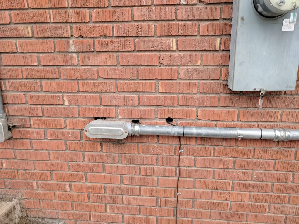 Spalled brick and worn mortar around conduit and the electrical meter on the temple's brick wall