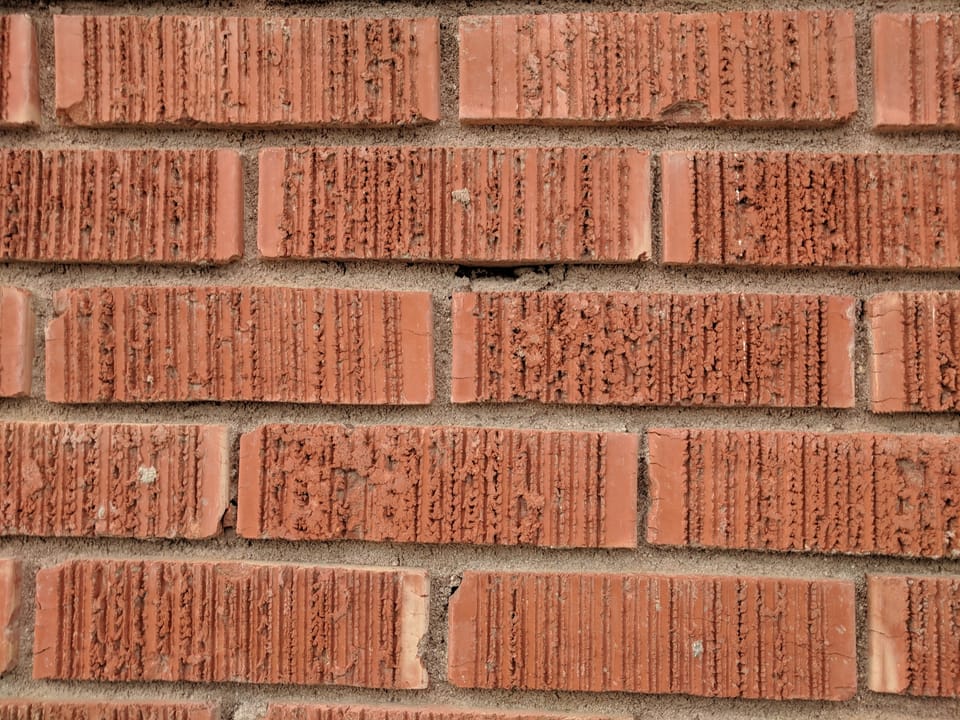 Close view of eroded and chipped brick faces and open joints on the temple's red brick wall
