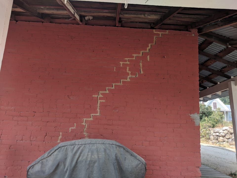 Long stair-step crack through painted brick wall under the porch roof, Miners Exchange, Idaho City