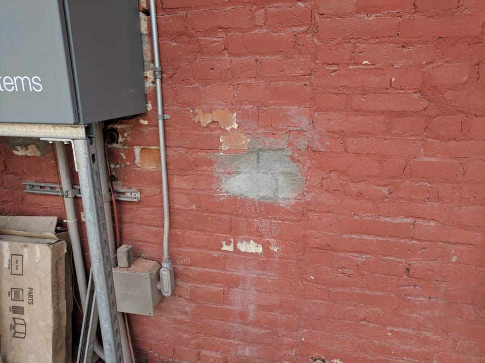 Spalled brick cut out and patched with fresh mortar beside conduit and an electrical panel