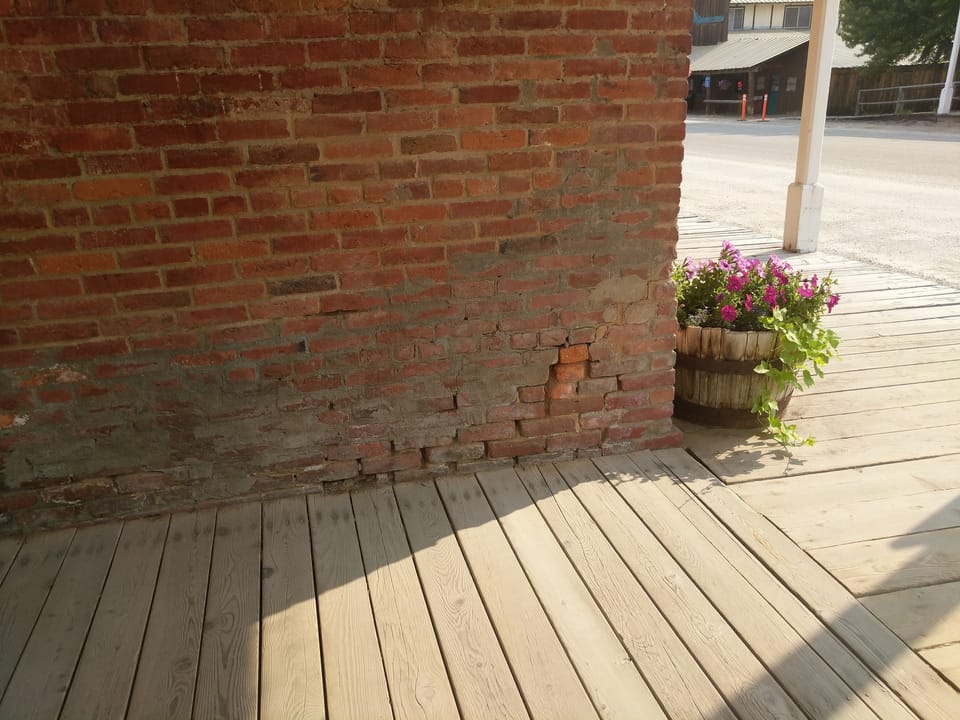 Eroded bottom brick courses meeting the wood boardwalk at the Miners Exchange, Idaho City