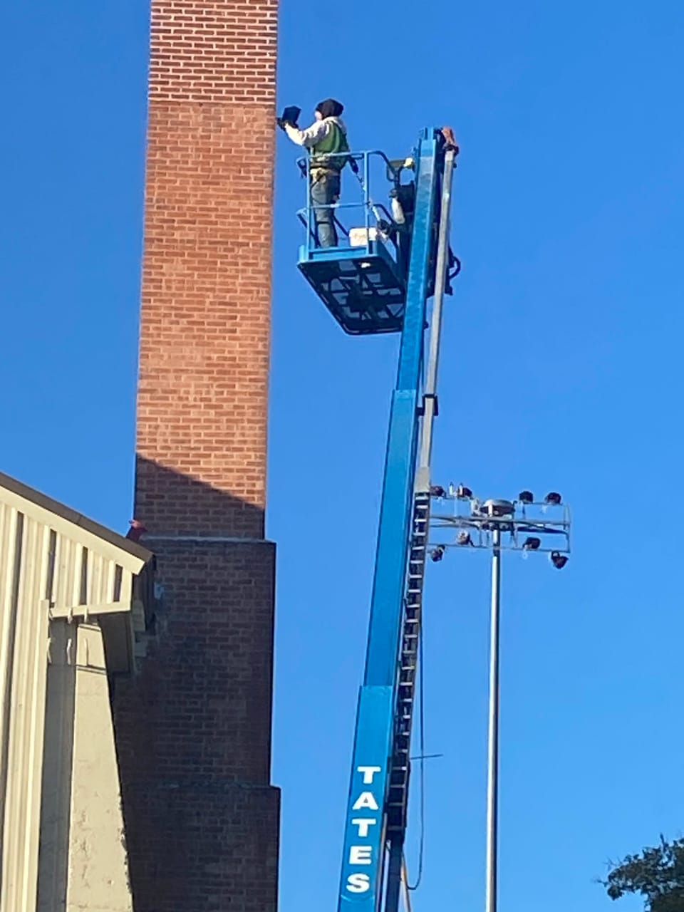 Mason in a boom lift basket repointing the tall brick chimney at Mountain Home Air Force Base