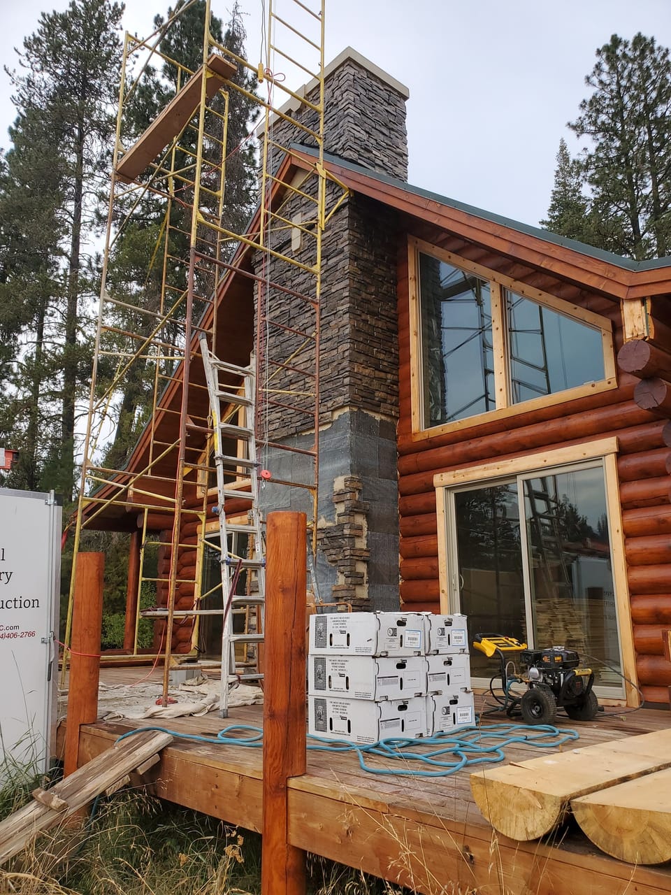 Stone veneer chimney nearly complete with boxes of stone stacked on the deck below the scaffold