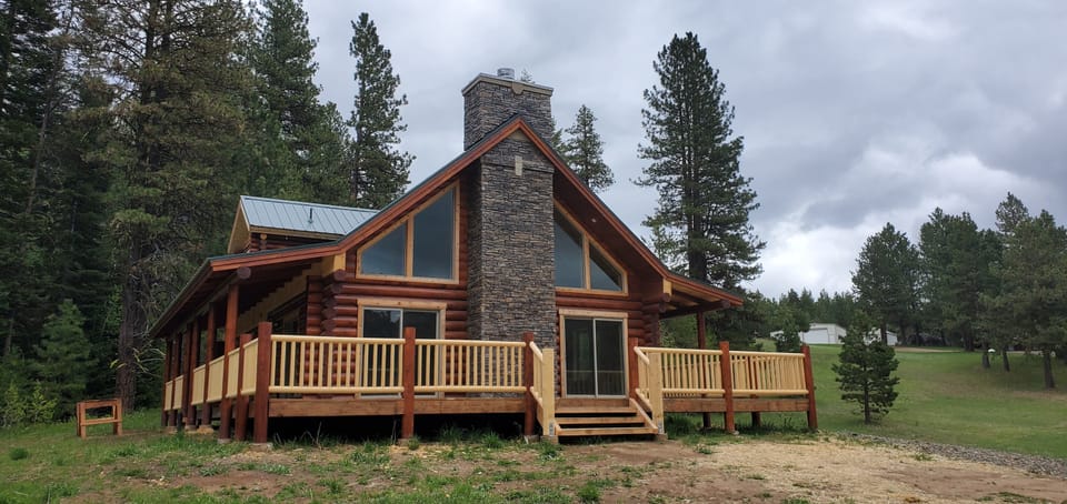 Log home with the completed grey stone veneer chimney running up the gable end above the deck