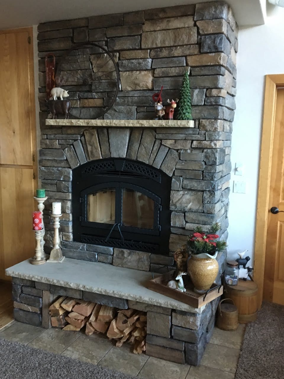 Floor-to-ceiling stacked stone fireplace with arched stone surround, mantel shelf, and hearth bench over wood storage