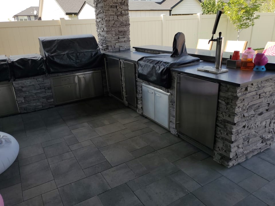 Finished outdoor kitchen in stacked stone veneer with stainless doors, tap tower and dark countertops