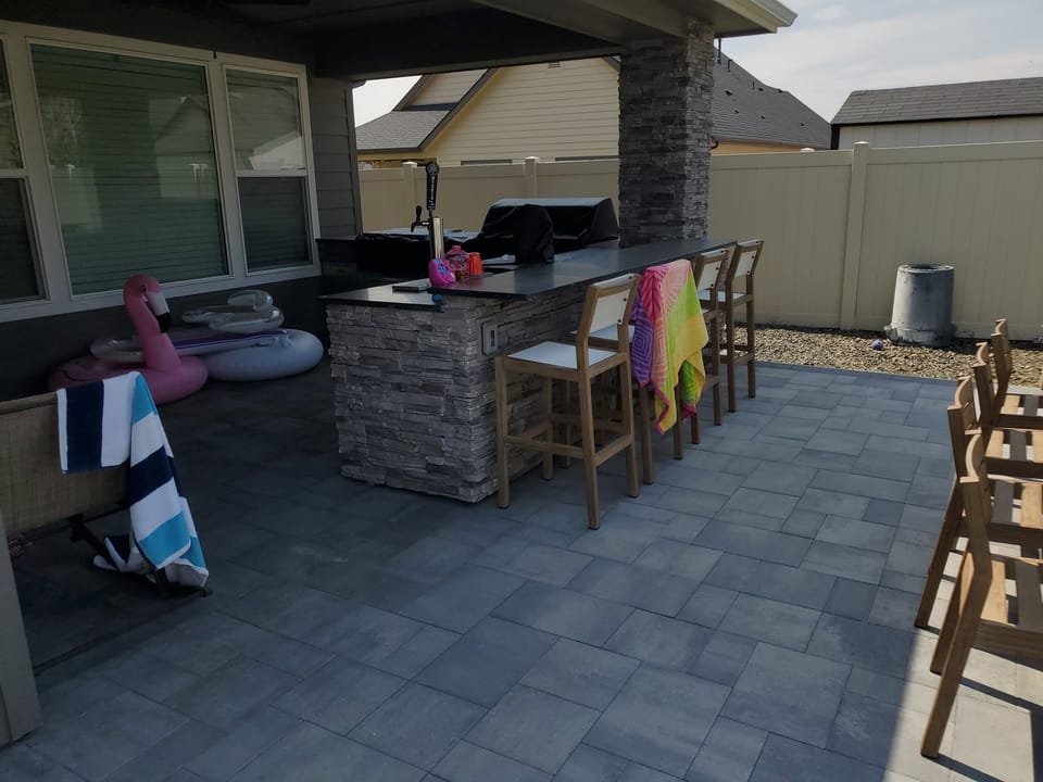 Stone-faced bar and beer tap on the paver patio with stools, grill and stone column behind
