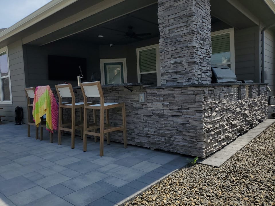 Stacked stone bar running along the covered patio with a matching stone column, bar stools pulled up