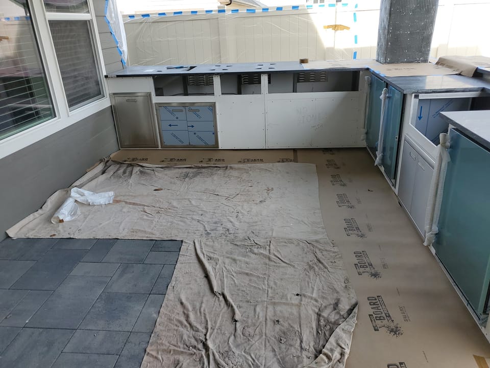 Dark countertops set on the outdoor kitchen frames with appliance cutouts, wrapped appliances and drop cloths around
