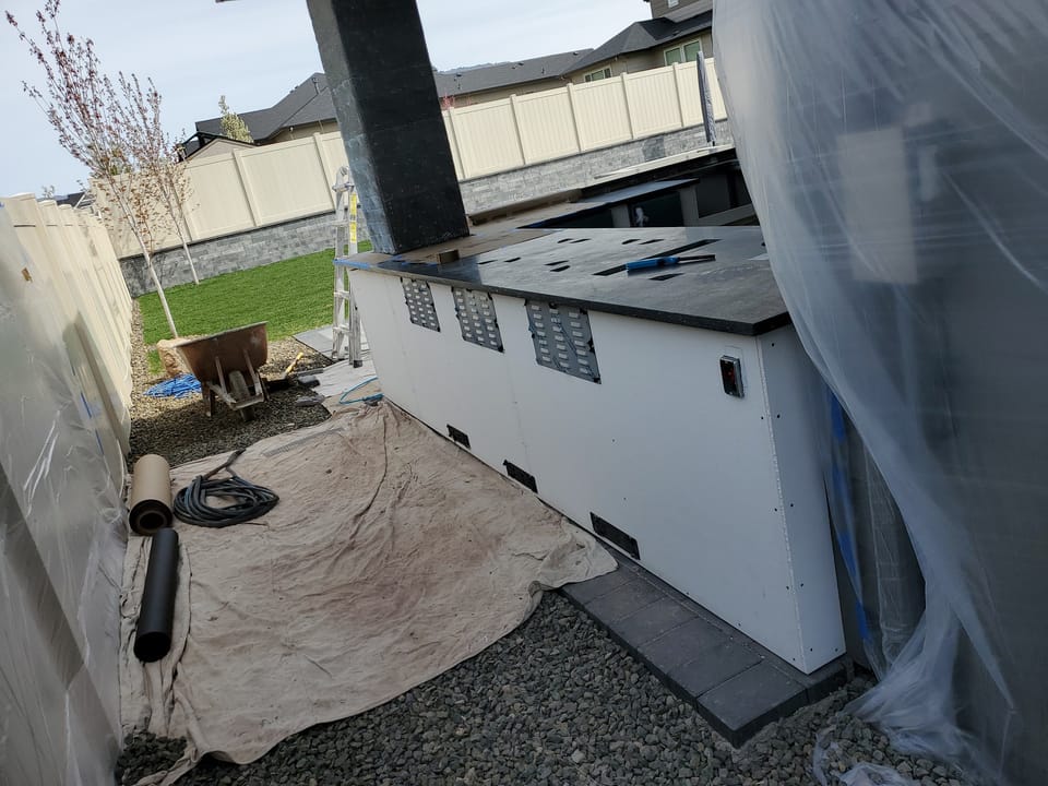 Back side of the outdoor bar with countertop set and vent openings framed, drop cloth and wheelbarrow alongside