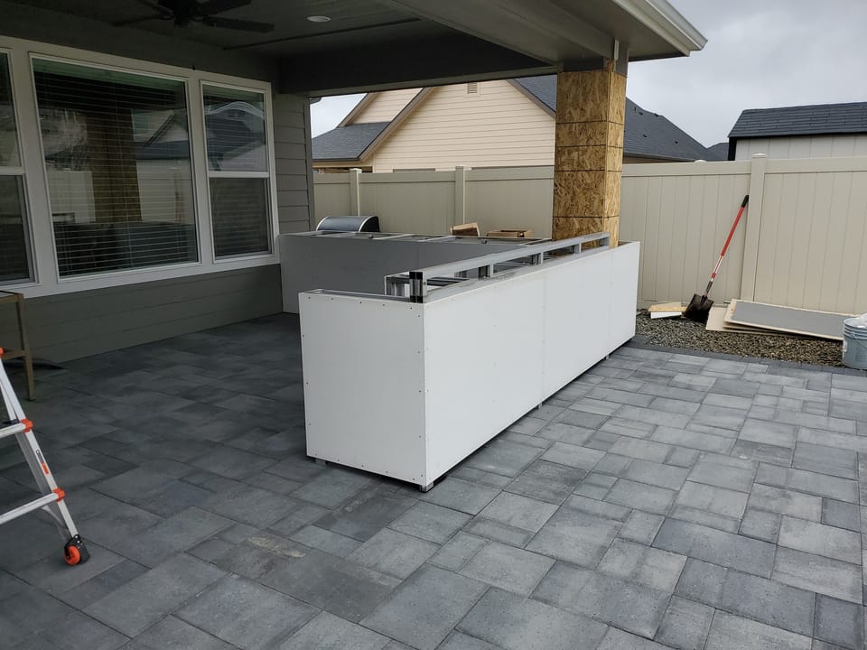 Bare outdoor kitchen cabinet frames standing on a gray paver patio before any stone veneer goes on