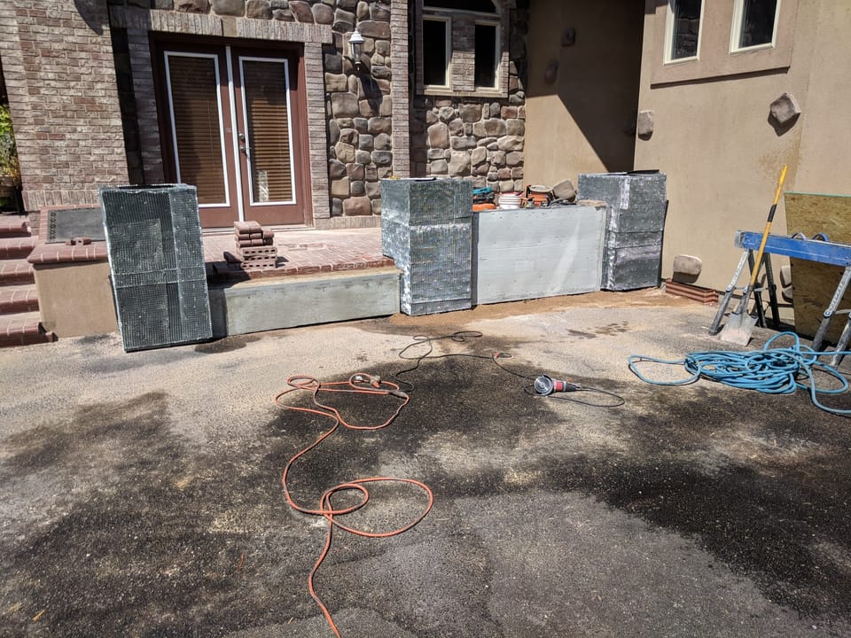 Poured concrete step and lath-wrapped planter boxes ready for stone veneer, tools and cords on the driveway