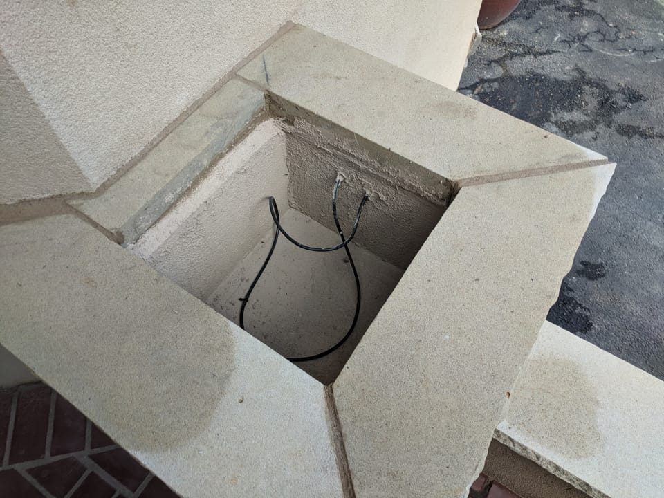Looking down into a finished stone planter box with cap stones, water line and drain run inside