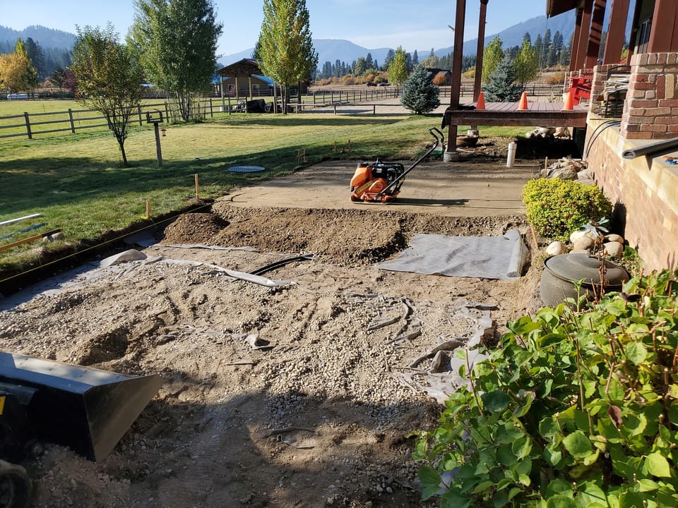 Thick crushed gravel base over fabric being compacted with a plate compactor before pavers go down